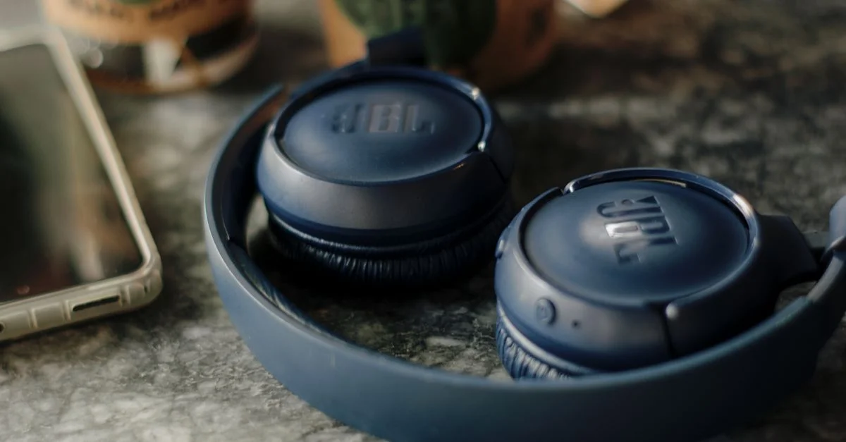 Écouteurs sans fil JBL bleu foncé à côté d'un smartphone et d'un café sur une table.
