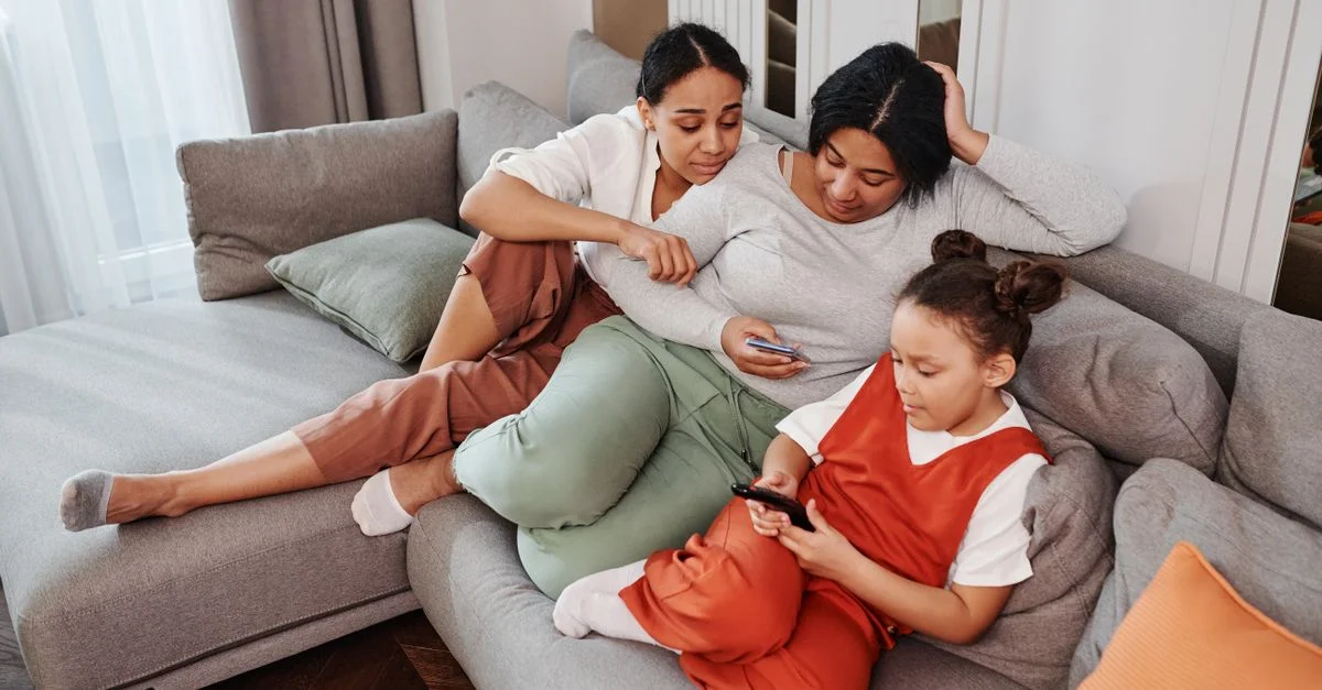 Une mère, une fille et un ami de la famille passent du temps de qualité ensemble sur un canapé dans le salon.