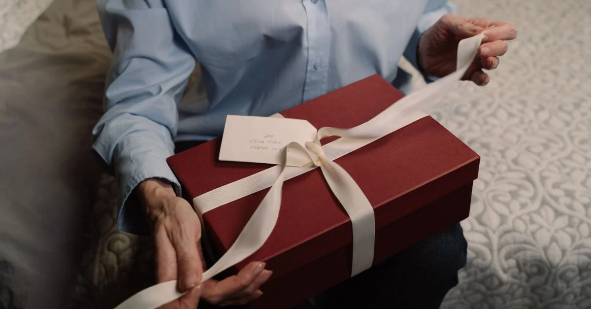 Une personne ouvre une boîte-cadeau rouge ornée d'un ruban blanc à l'intérieur, créant un moment chaleureux et personnel.