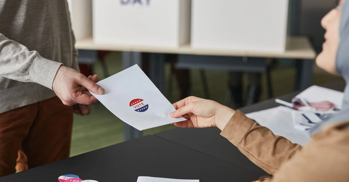 Deux personnes échangeant un bulletin de vote lors d'un processus de vote en intérieur.
