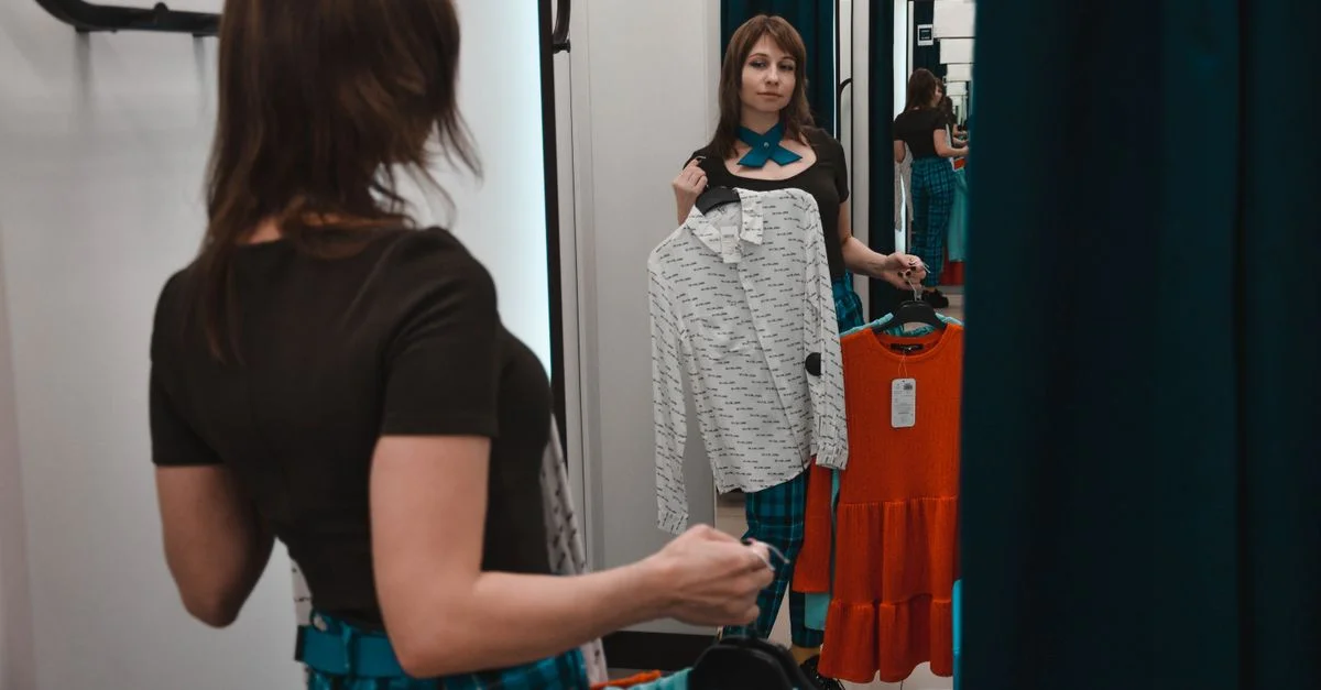Une femme dans une cabine d'essayage sélectionnant entre deux tenues dans une boutique.