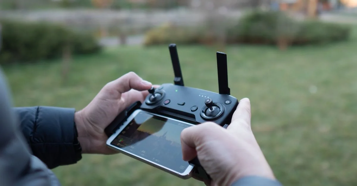 Gros plan sur des mains utilisant une télécommande de drone avec un smartphone attaché dans un cadre extérieur.