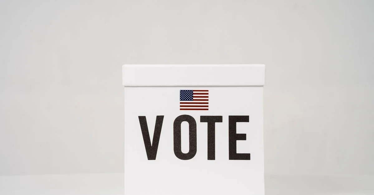 Une urne électorale minimaliste avec 'Vote' et un drapeau américain, symbolisant les élections.