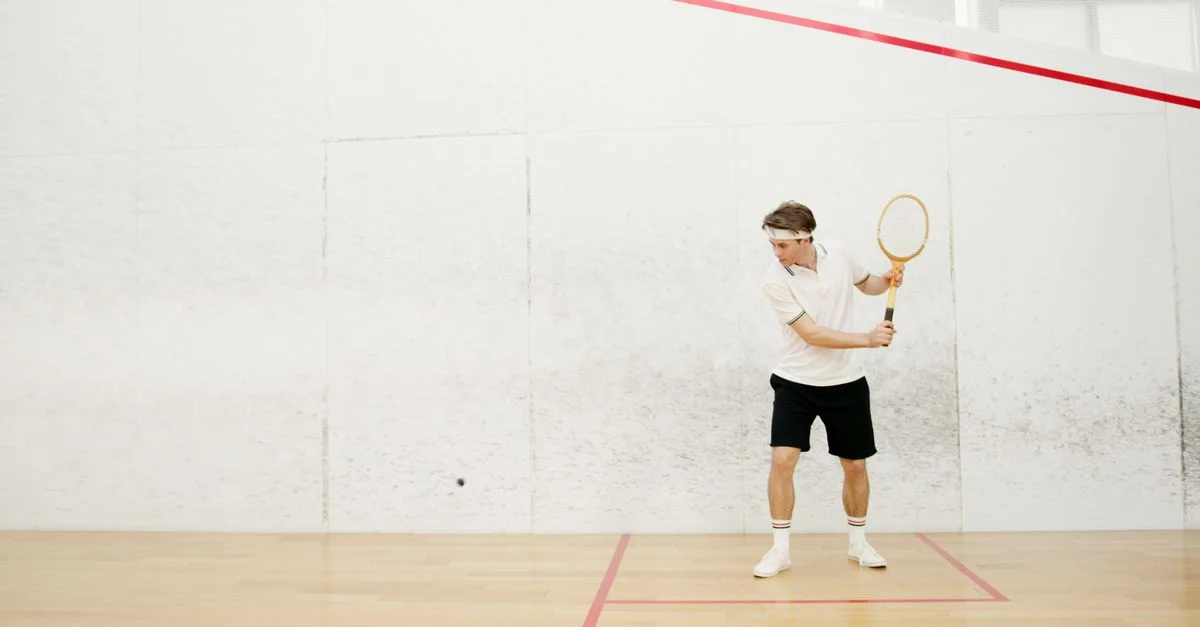 Un joueur de squash masculin en action, prêt à frapper une balle sur un court de squash intérieur.